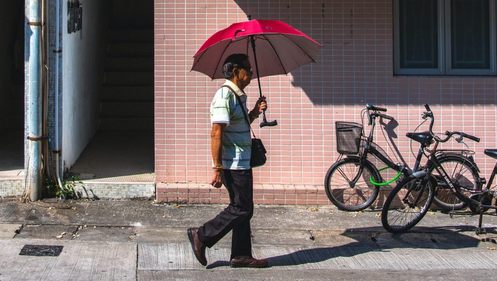 Man on street holding umbrella walking beneath an air conditioner