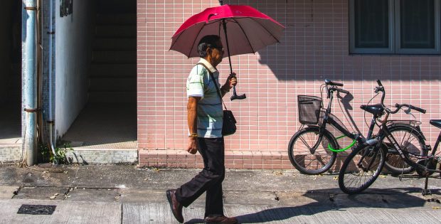 Man on street holding umbrella walking beneath an air conditioner