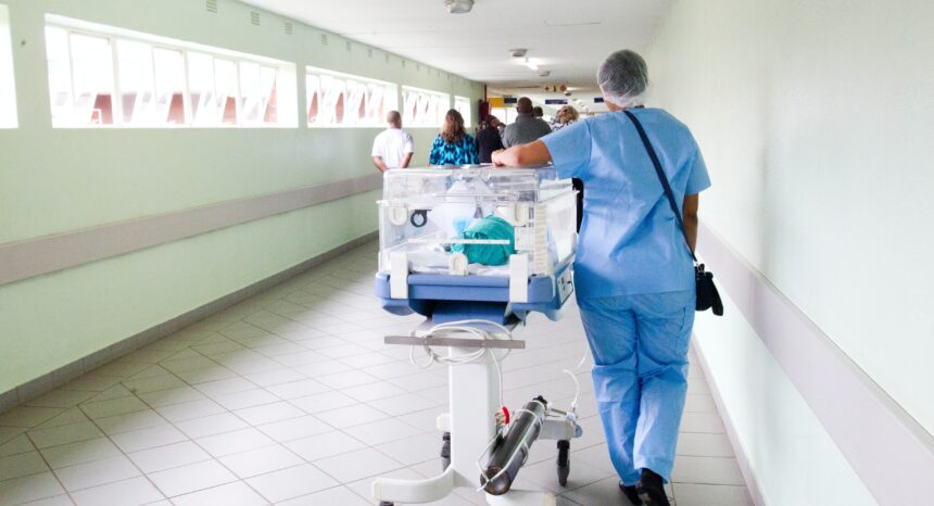 Nurse rolling a baby incubator down hospital hall
