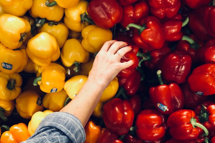 Arm reaching to pick a red bell pepper from a bunch of red and yellow bell peppers
