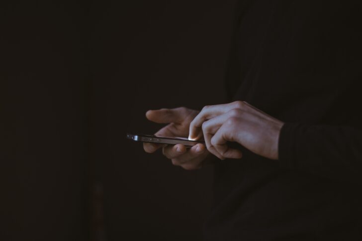 Two hands holding an iphone against a black background.
