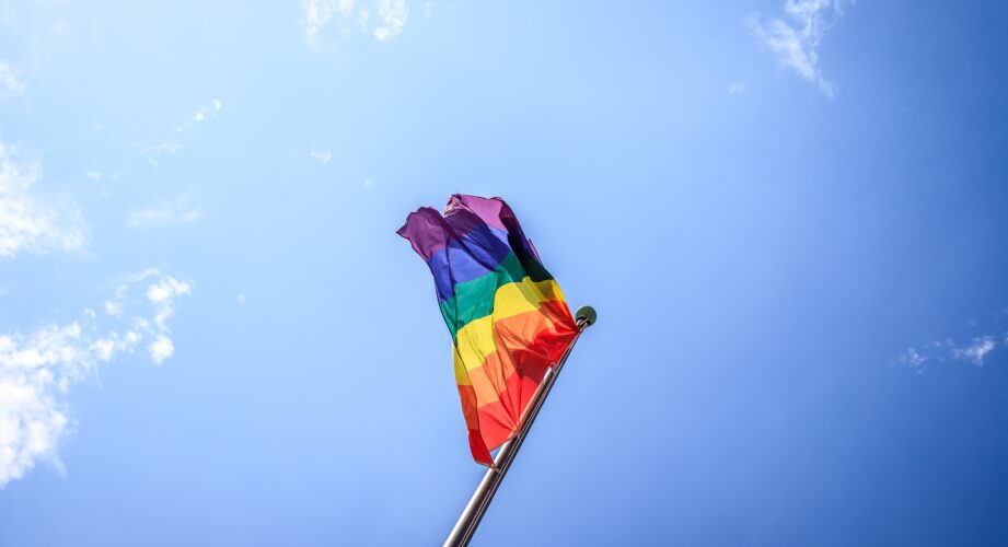 A rainbow flag against a blue sky.