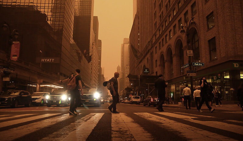 Orange-color photo of people walking across the street at 42nd St. at Grand Central Terminal in New York City.