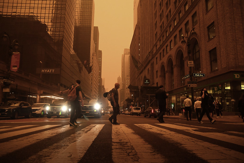 Orange-color photo of people walking across the street at 42nd St. at Grand Central Terminal in New York City.