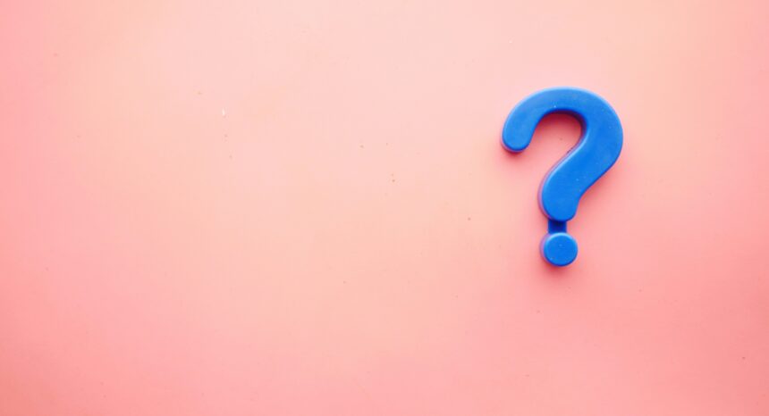 Blue plastic question mark on a plain light pink background, positioned on the right with lots of empty space on the left.