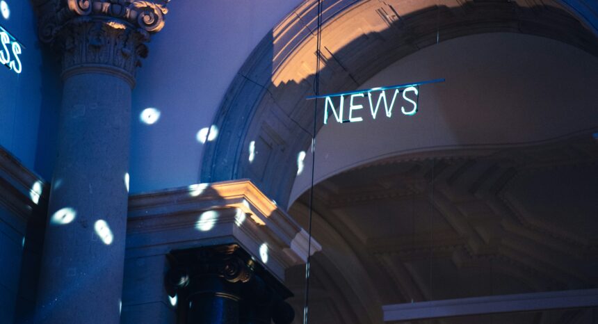 Neon “NEWS” sign hanging inside a grand, columned building with blue lighting and scattered light reflections on the walls and pillars.
